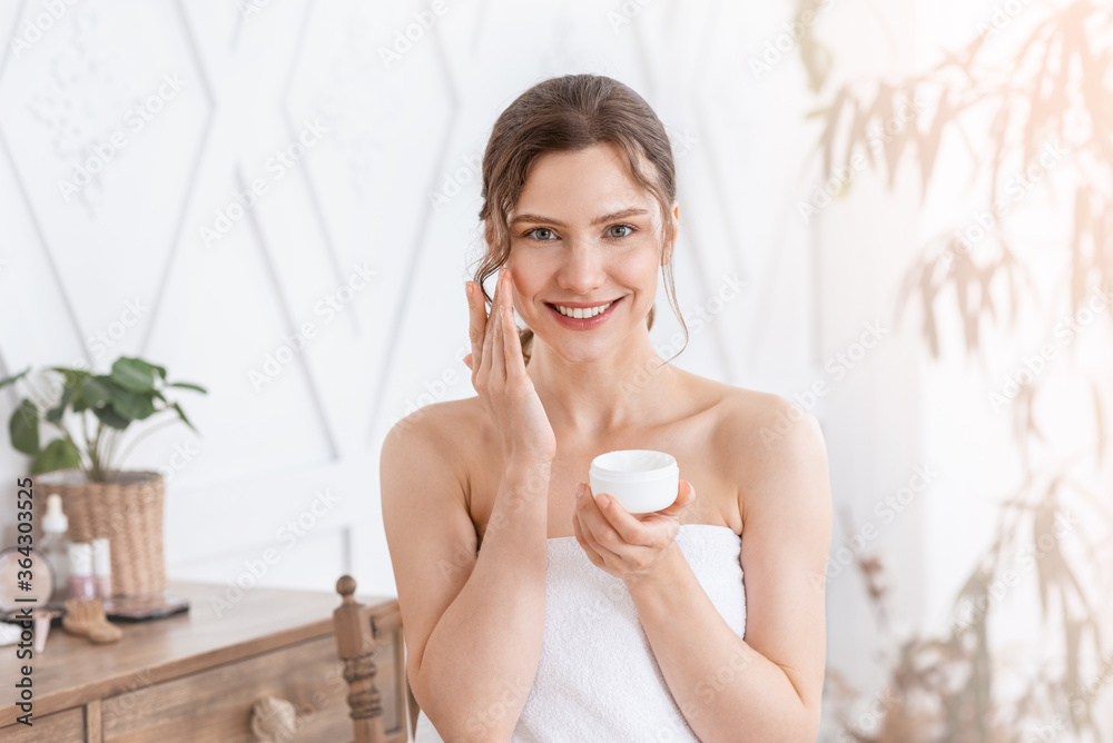 Attractive young woman applying face cream at home Attractive young woman applying face cream at home