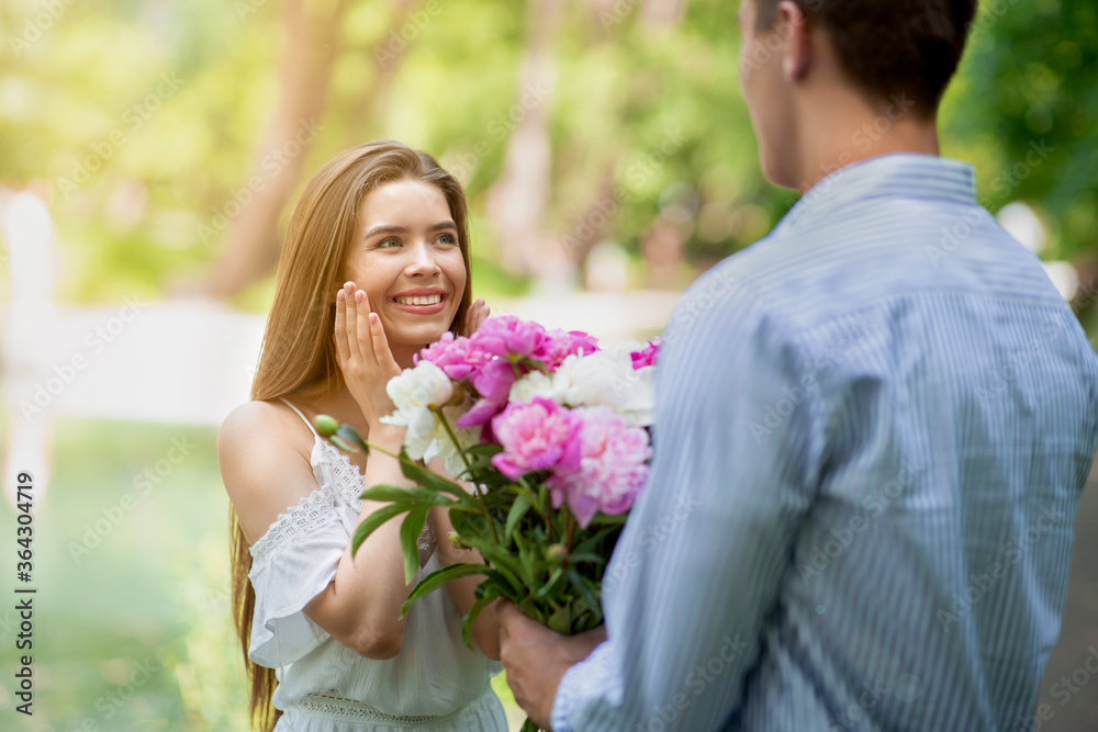 Affectionate young guy surprising his girlfriend with flower bouquet outside Affectionate young guy surprising his girlfriend with flower bouquet outside