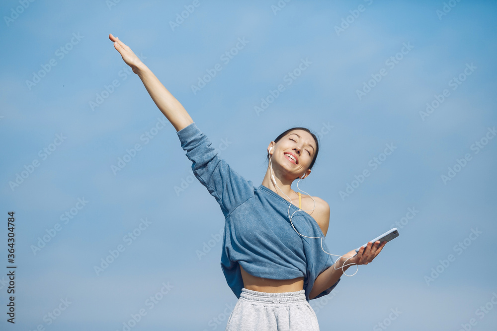 Beautiful girl standing on a sky background. Woman in a blue sweater. Lady with phone in her hands Beautiful girl standing on a sky background. Woman in a blue sweater. Lady with phone in her hands