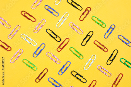 paper clips in different colors on a yellow background are laid out in straight rows, an abstraction