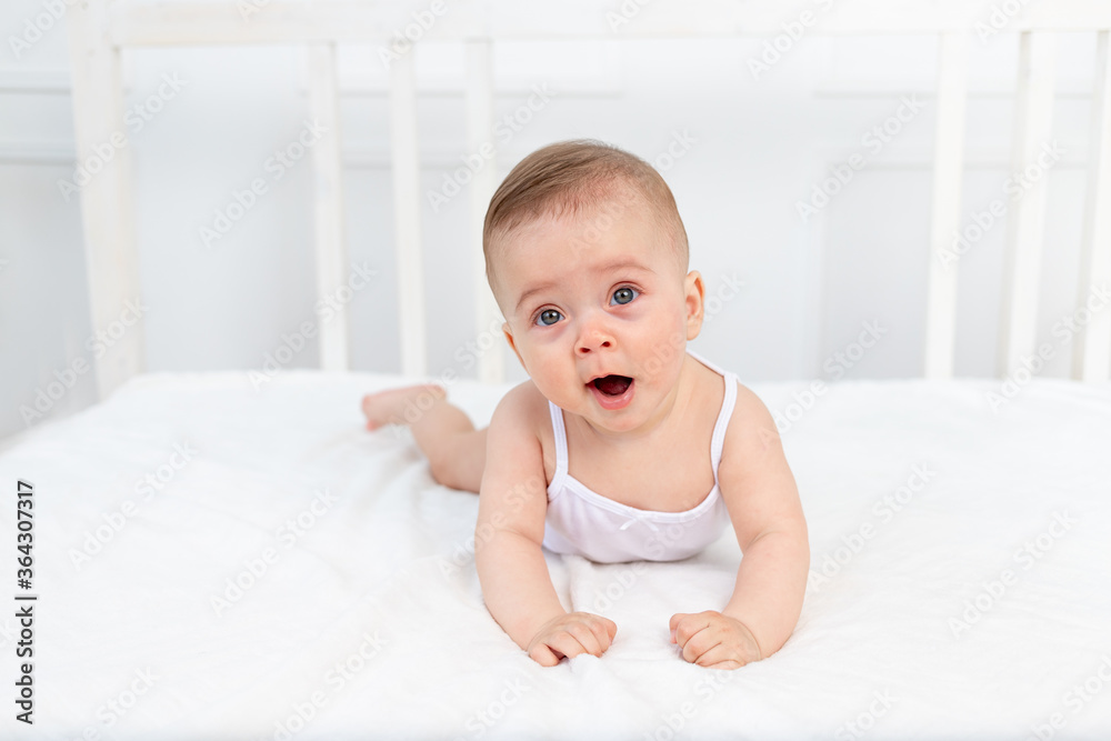 baby girl 6 months old lying on the bed in the nursery on her stomach and yawning, baby morning, baby products concept baby girl 6 months old lying on the bed in the nursery on her stomach and yawning, baby morning, baby products concept