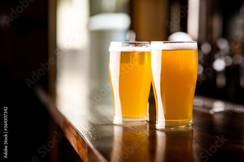 Friends meeting at pub. Two glasses of light beer with foam on wooden bar in pub
