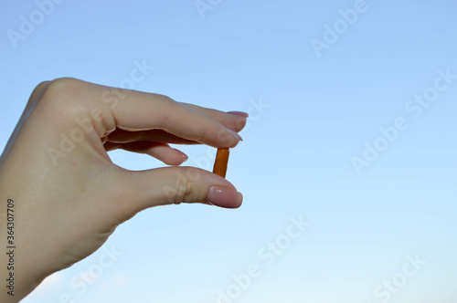 woman with manicure holds in her fingers a brown oval tablet against a blue sky for taking medicine inside. drug therapy for the treatment of viral infections, hand shadow with the drug
