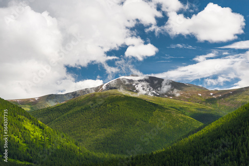 Mountains and forests of the Altai against the blue sky with clouds