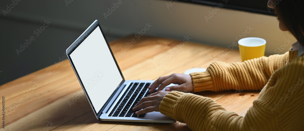 A woman is typing on a white blank screen computer laptop that putting on a wooden working desk. - obrazy, fototapety, plakaty 