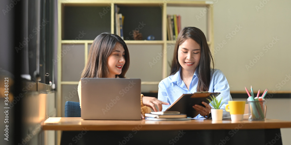 Women are working together with a computer laptop and clipboard at the wooden working desk. Women are working together with a computer laptop and clipboard at the wooden working desk.