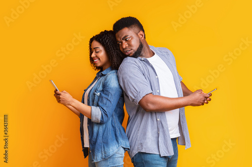 Distrust Concept. Jealous black man peeking into girlfriend's cellphone over shoulder