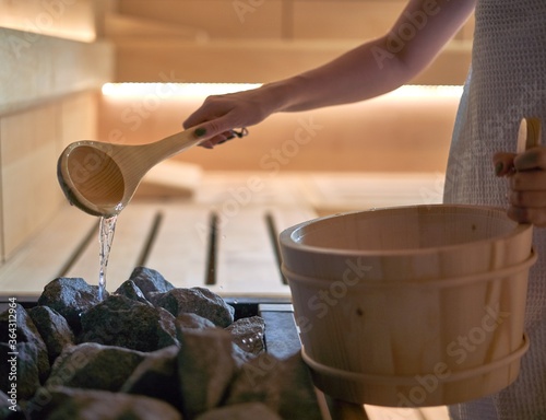 Woman pouring water into hot stone in sauna room.