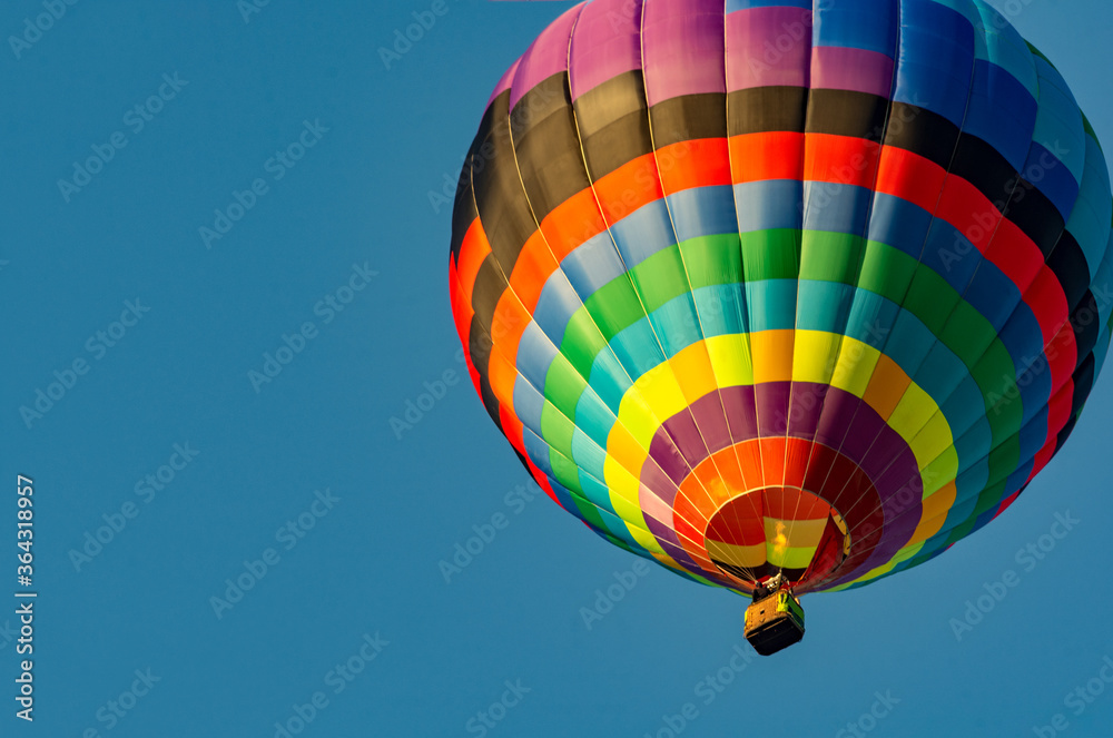 Naklejka premium Balloon flying high in the sky. Balloon basket with people. Aeronautic sport. Burning gas. Bright multi-colored balloon. Romantic trip. Free space for text.