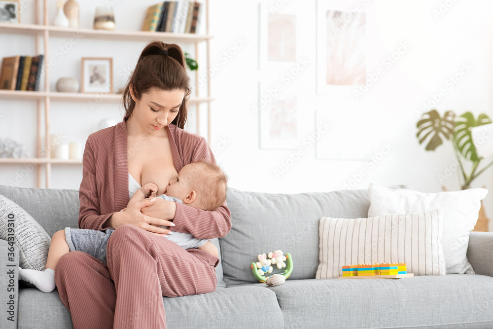 Breastfeeding Concept. Young woman lactating her toddler baby on couch at home Breastfeeding Concept. Young woman lactating her toddler baby on couch at home