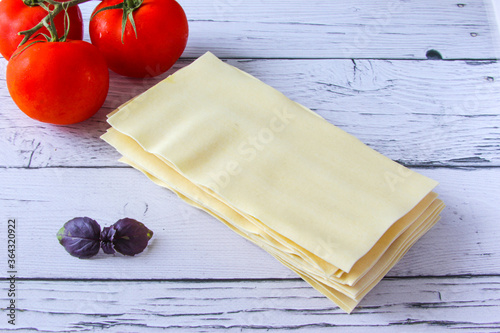 Lasagne sheets pasta with tomato and basil leaf on a wooden background. Ingredients for an italian recipe. Copy space. photo