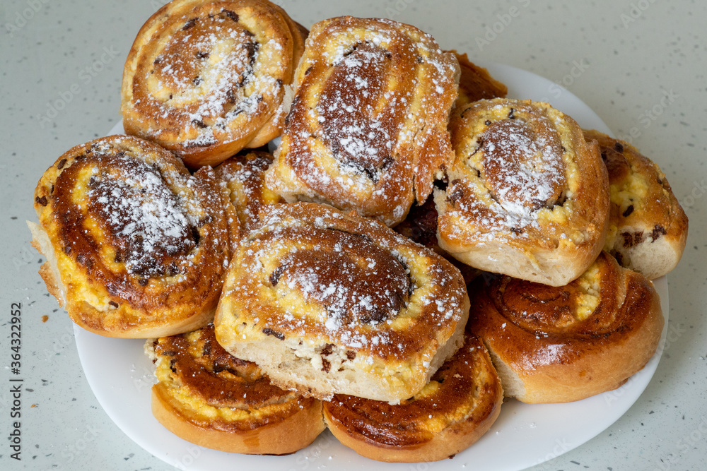 Patties with cottage cheese and raisins piled up on a white plate. Pies sprinkled with powdered sugar