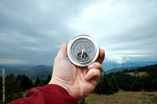 Close-up Male hand and silver compass on a background of mountain landscape. The concept of travel, hiking, help, searching, vacation. Copy space.