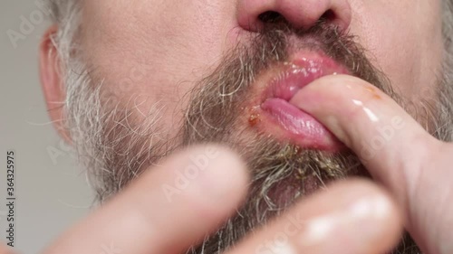 Close up of man's bearded face chewing chicken and licking fingers soiled with food.