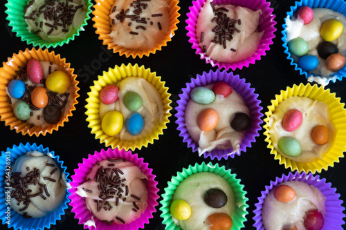 Delicious pastry cooked at home. Homemade cupcakes in multi-colored silicone molds and with colored chocolates inside on a baking tray.