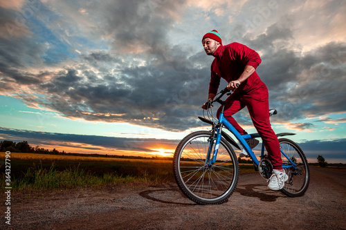 Sports training on a bicycle. A man in a tracksuit on a sunset background. The concept of a healthy lifestyle, cardio training, physical activity. Copy space.