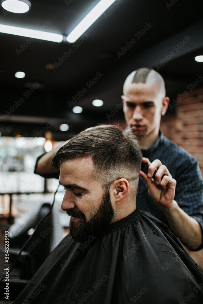 Good looking young adult man getting a hair and beard styling and dressing treatment by professional hairstylist. Good looking young adult man getting a hair and beard styling and dressing treatment by professional hairstylist.