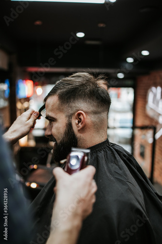 Good looking young adult man getting a hair and beard styling and dressing treatment by professional hairstylist.