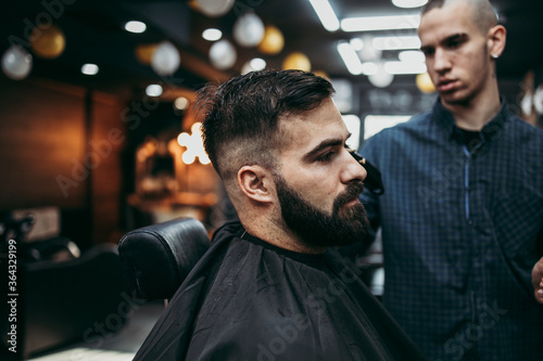 Good looking young adult man getting a hair and beard styling and dressing treatment by professional hairstylist.