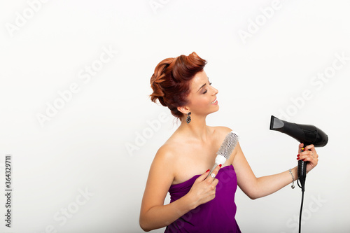 Beautiful woman taking care of her red hair. Attractive young girl using hairdryer and hairbrush for her very stylish haircut.