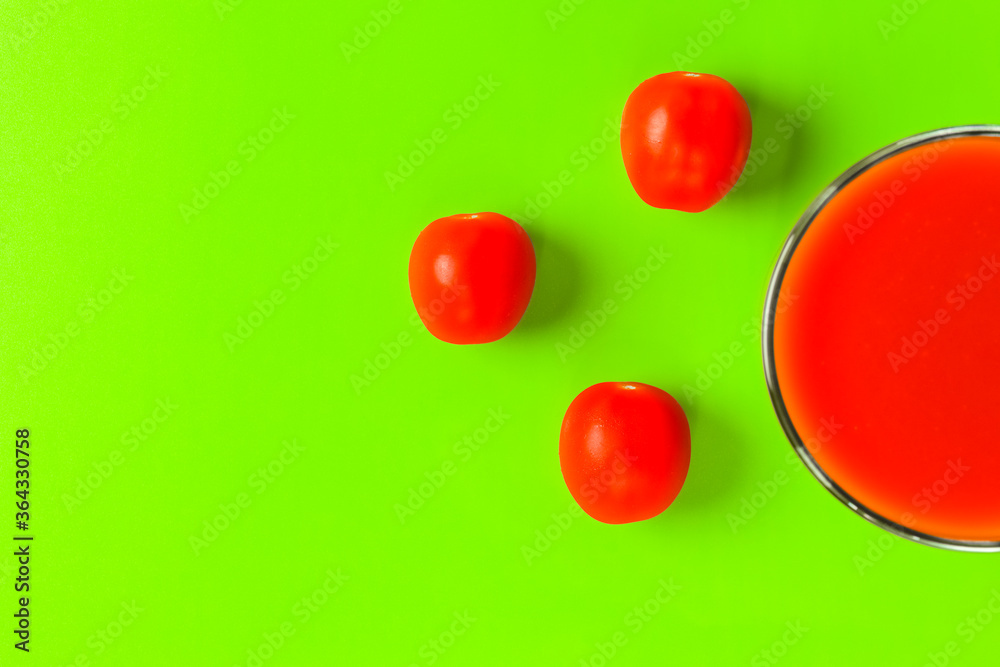 red tomato and a glass of tomato juice on a green background. hard shadow. isolate red tomato and a glass of tomato juice on a green background. hard shadow. isolate