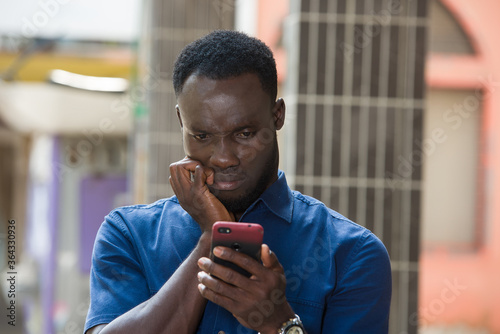 Close-up of a young man with mobile phone, thoughtful.