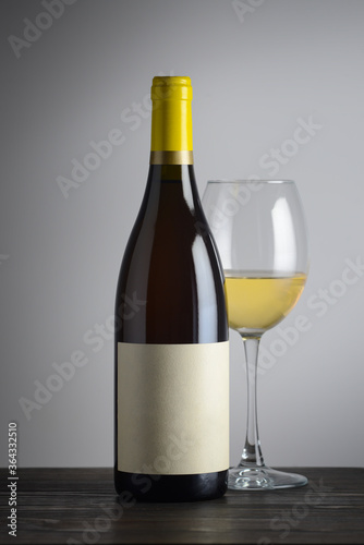 sealed bottle of white wine near a glass of wine on a wooden table. Place for text