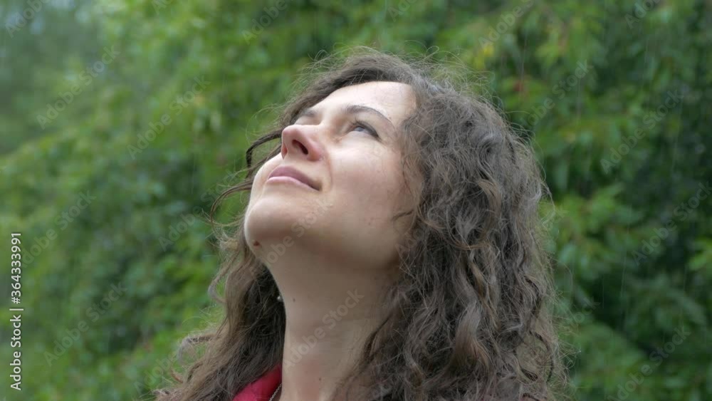 The girl enjoys the summer rain. Looking up at the drops and clouds. In a red cloak. Face. The girl enjoys the summer rain. Looking up at the drops and clouds. In a red cloak. Face.