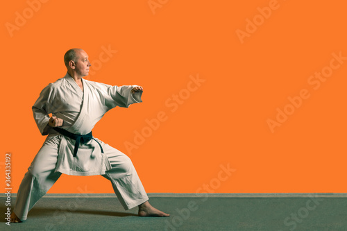 A karate man in a white kimono with a black belt makes kata.