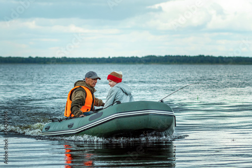 Grandfather and grandson ride a motor boat on the lake. The concept of family, summer vacation, generation. Copy space.