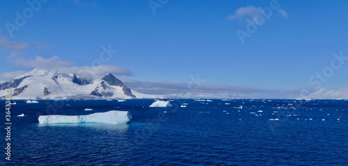 Iceberg in blue Antarctic sea, before mountain with blue sky and sun, Antarctica