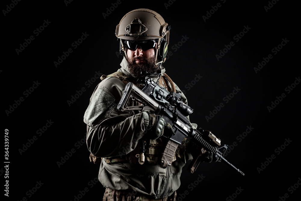 American commando in a military uniform with a weapon looks at copy space, a marine on a dark background, a member of the elite troops, war concept American commando in a military uniform with a weapon looks at copy space, a marine on a dark background, a member of the elite troops, war concept