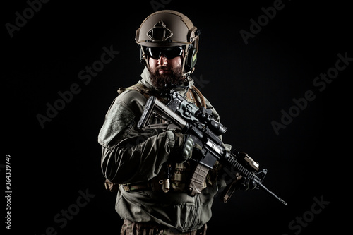 American commando in a military uniform with a weapon looks at copy space  a marine on a dark background  a member of the elite troops  war concept