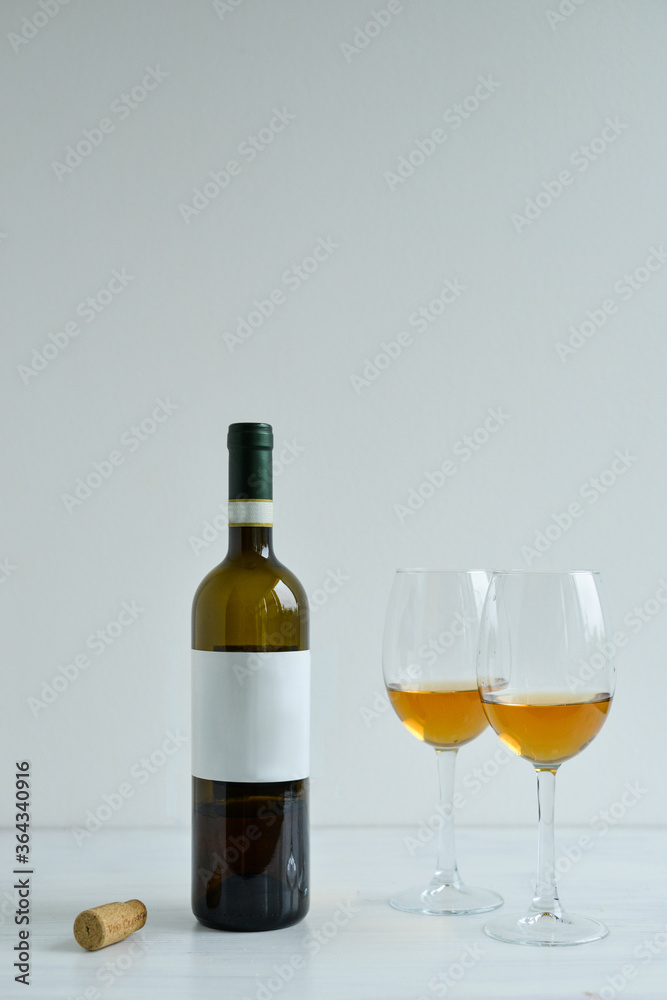 Bottle and two glasses of white wine standing on the white table Bottle and two glasses of white wine standing on the white table
