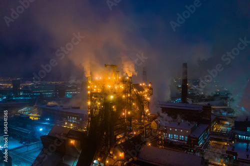 Night top view of steel plant at night with smokestacks and fire blazing out of the pipe. Industrial panoramic landmark with blast furnance of metallurgical production
