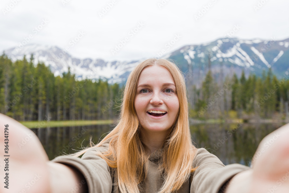 The girl tourist taking selfie in the mountain lake. Looking at camera and smile. Travel and active life concept. Outdoors The girl tourist taking selfie in the mountain lake. Looking at camera and smile. Travel and active life concept. Outdoors