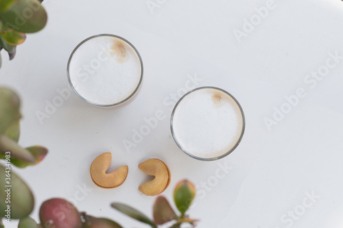 Two Glasses of coffee with cream and two fortune cookies near the leaves on white background