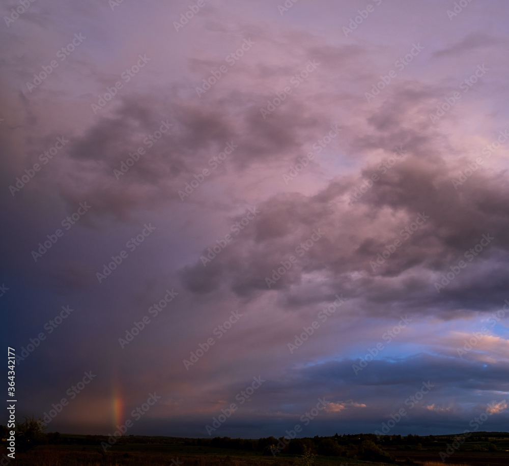 Spring meadow after rain, cloudy evening pre sunset sky with rainbow, rural hills and fields in far. Natural seasonal, weather, climate, countryside beauty concept scene. Spring meadow after rain, cloudy evening pre sunset sky with rainbow, rural hills and fields in far. Natural seasonal, weather, climate, countryside beauty concept scene.
