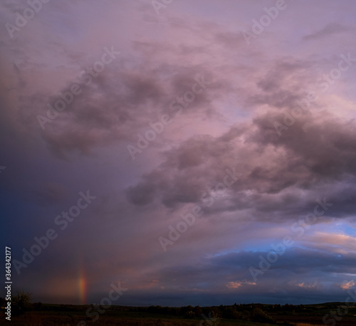 Spring meadow after rain, cloudy evening pre sunset sky with rainbow, rural hills and fields in far. Natural seasonal, weather, climate, countryside beauty concept scene. © wildman