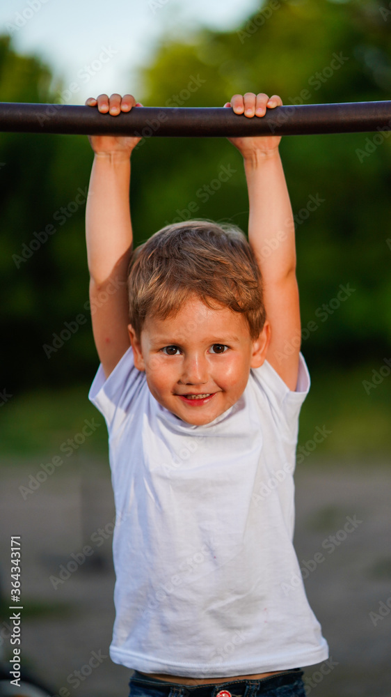 Portrait of cute little boy hanging on horizontal bar in summer park