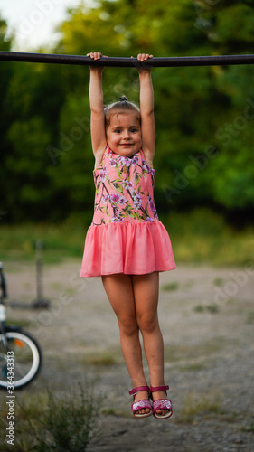 Portrait of funny little girl hanging on horizontal bar in summer park