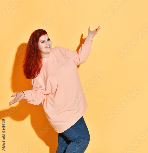 Excited smiling young chubby lady is happy of her achievement, showing voila gesture with open palms. Studio shot isolated on orange photo