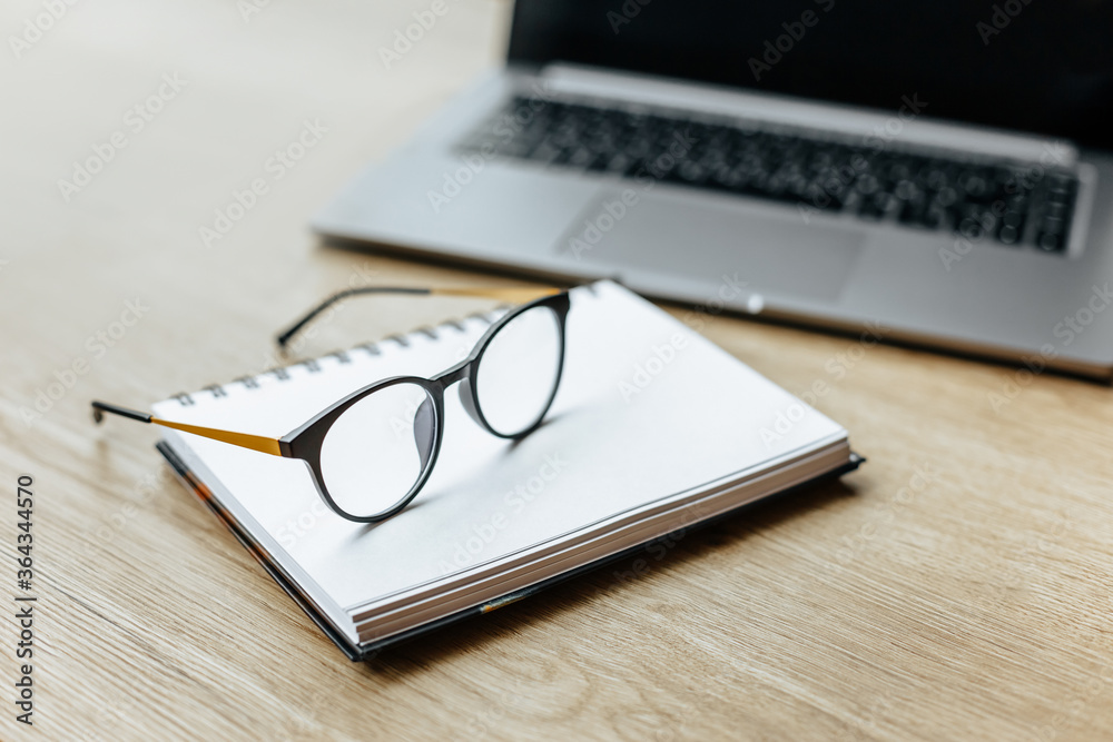 Glasses at the workplace in the office near the laptop and notepad. Business hours Glasses at the workplace in the office near the laptop and notepad. Business hours