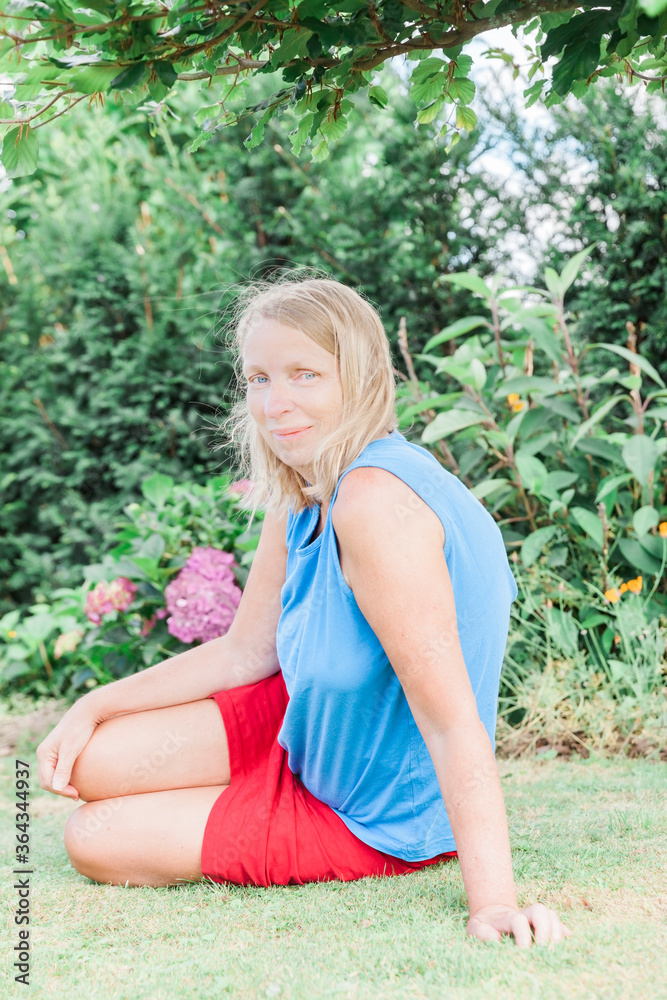 Mature woman sitting on meadow in garden Mature woman sitting on meadow in garden