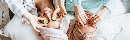 Two girls make homemade face and hair beauty masks. Cucumbers for the freshness of the skin around the eyes. Women take care of youthful skin. Girlfriends laugh at home lying on the floor on pillows.