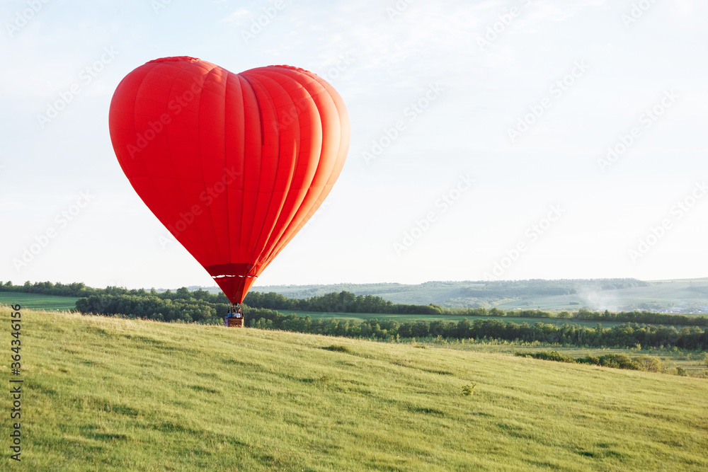 Fototapeta premium Hot air balloon in the shape of a heart is landing on the green valley