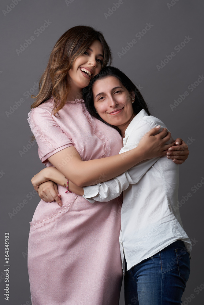 Fototapeta premium Two women are hugging on grey background with copy space