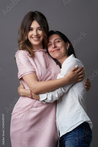 Two women are hugging on grey background with copy space