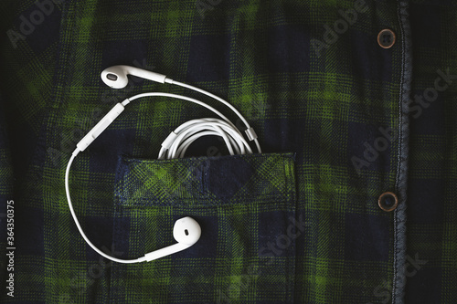 Overhead shot of the wired in-ear white headphones coming out of the chest pocket on the checkered shirt photo