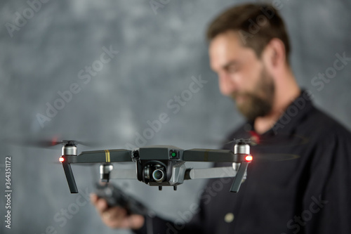 Happy man testing quadcopter. Remote unmanned aerial vehicle with camera. Male holding radio controller. Modern entertainment. Selective focus. A young adult man plays with a quadrocopter and has fun.